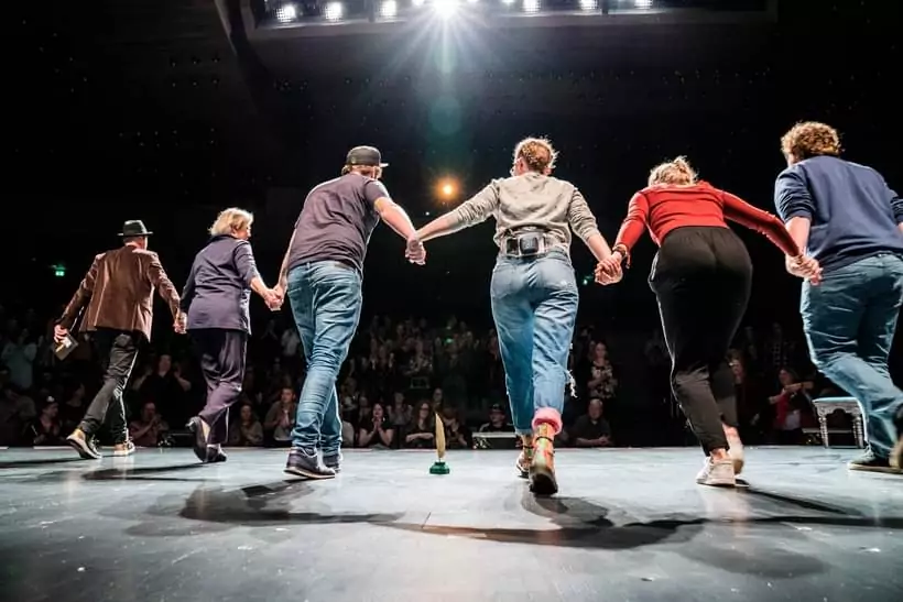 Poetry Slam Performer:innen Hand in Hand beim gemeinsamen Bühnenabgang vor Publikum, Abschlussapplaus eines Auftritts mit Luise Wolff
